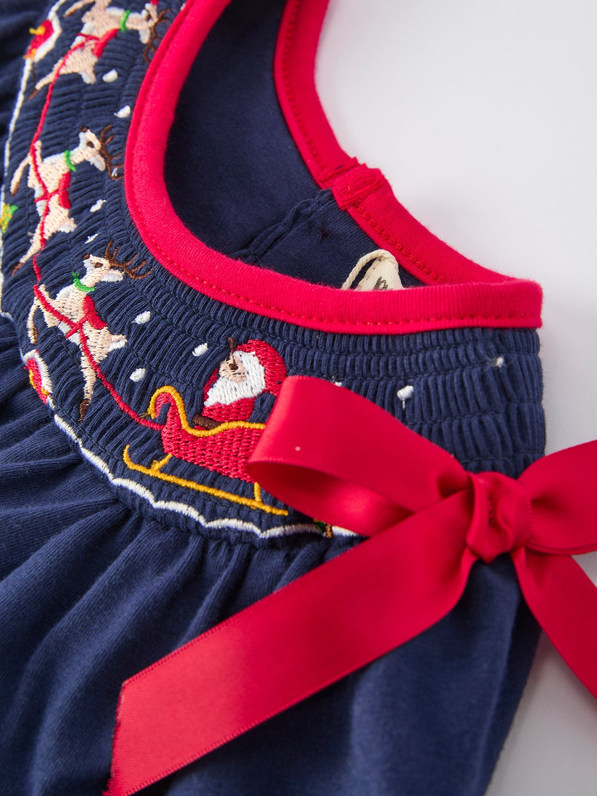 Navy baby girls Christmas romper featuring embroidered Santa sleigh, reindeer, and a festive red bow trim.