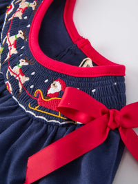 Navy baby girls Christmas romper featuring embroidered Santa sleigh, reindeer, and a festive red bow trim.