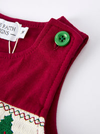 Red baby romper shoulder with green button, displaying smocking and Christmas tree embroidery detail.