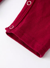 Close-up of red baby romper leg with silver snap buttons and reinforced stitching for easy dressing.