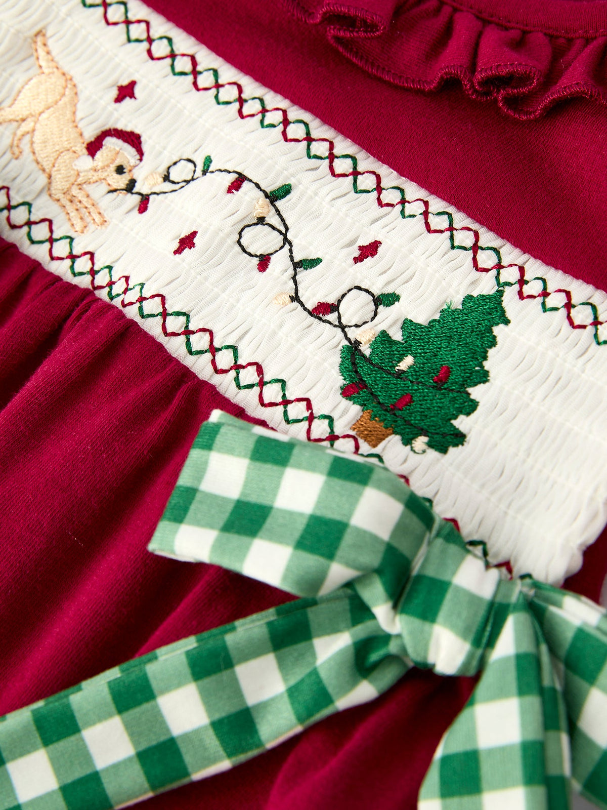 Red baby romper with festive embroidered reindeer, Christmas tree, and green plaid bow on smocked white panel.