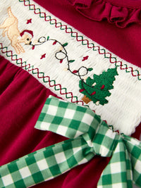 Red baby romper with festive embroidered reindeer, Christmas tree, and green plaid bow on smocked white panel.