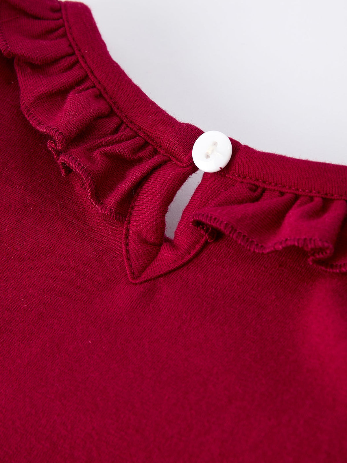 Close-up of burgundy baby romper with ruffled neckline and white button detail for festive holiday wear.