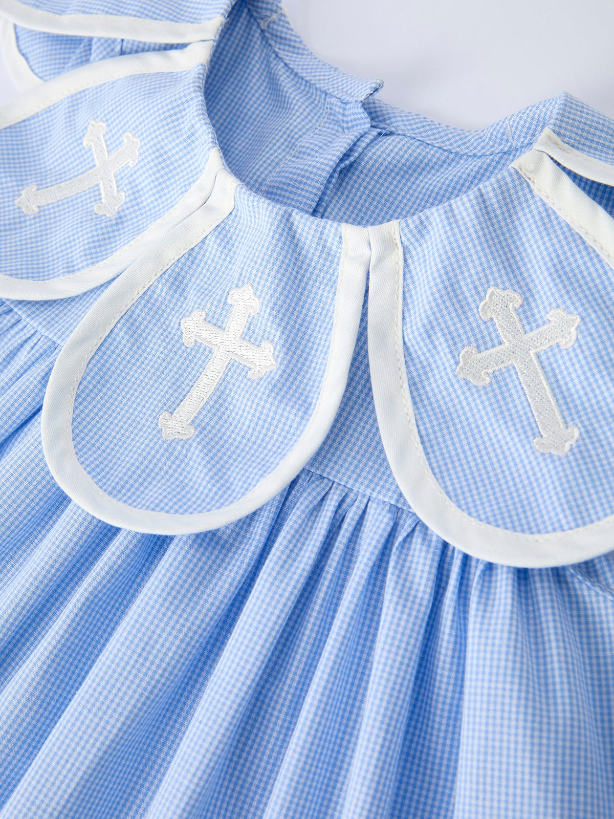 Blue gingham christening dress with white trimmed bishop collar featuring cross embroidery (close-up).