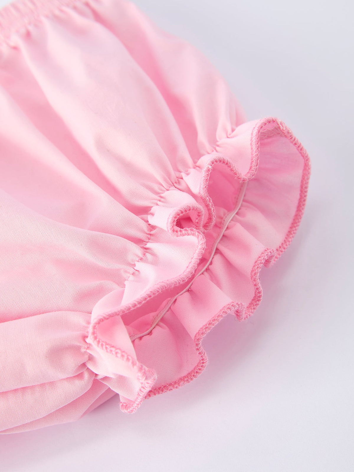 Close-up of pink fabric with ruffled trim from a floral smocked bishop bloomer set.