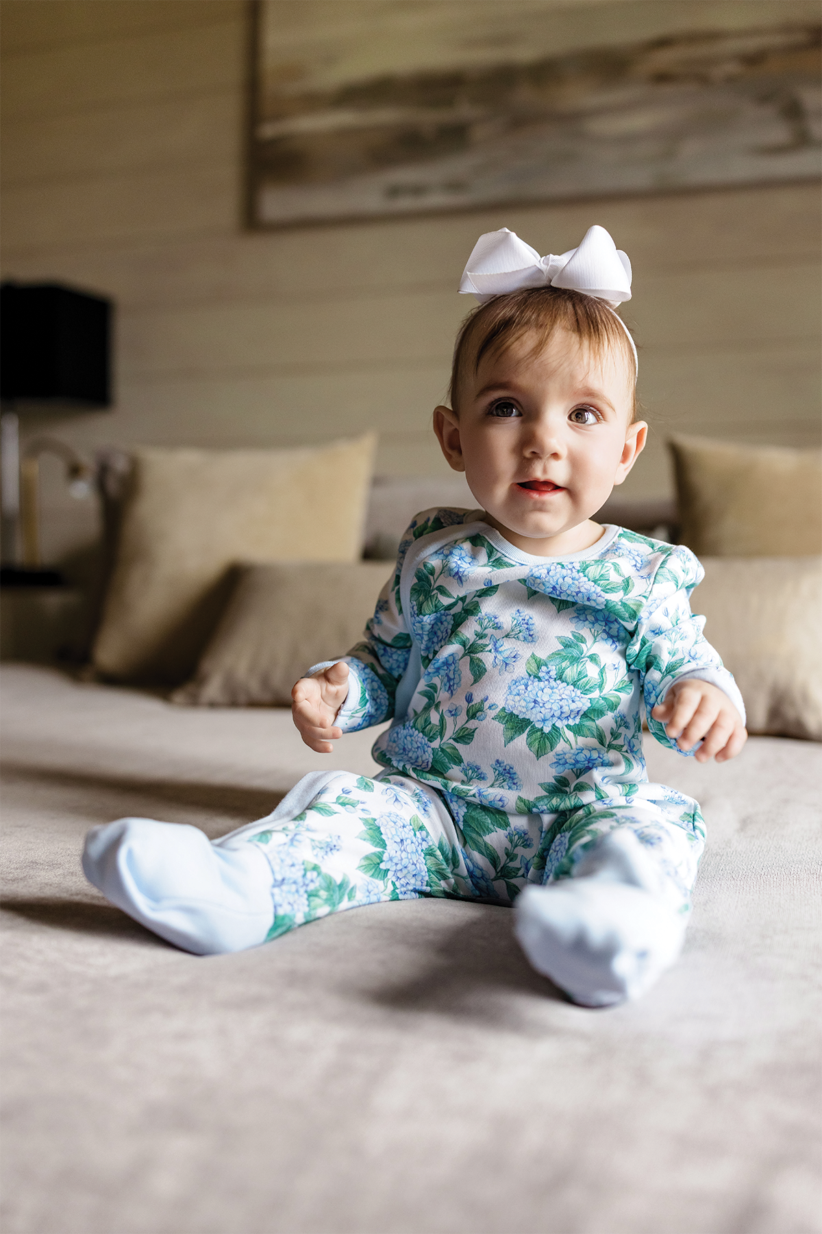 Baby wearing Hydrangea Heaven organic cotton pajama set with blue hydrangea print and white bow headband.