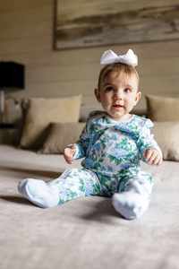 Baby wearing Hydrangea Heaven organic cotton pajama set with blue hydrangea print and white bow headband.