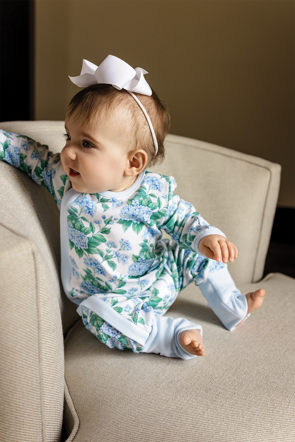 Baby wearing Hydrangea Heaven organic cotton pajama set with blue-green hydrangea print and white bow headband.