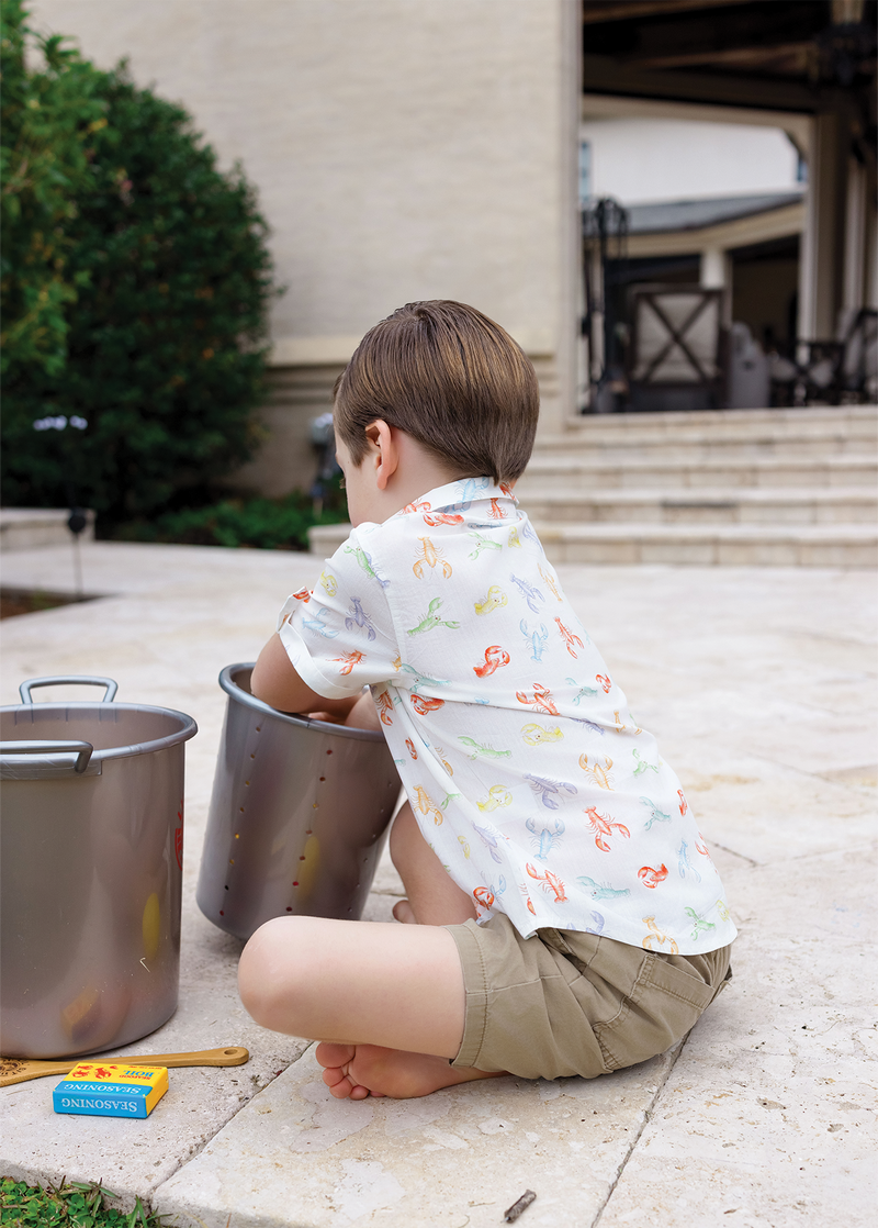 Child sitting on a stone pavement with pots and pans, wearing a patterned shirt and shorts.