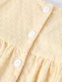 Close-up of cream dotted fabric with white buttons from Farm Girl Chicken Smocked Bow Ruffle Dress.