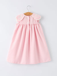 Pink gingham christening dress for girls with white-trimmed shoulder patches featuring cross embroidery, on hanger.