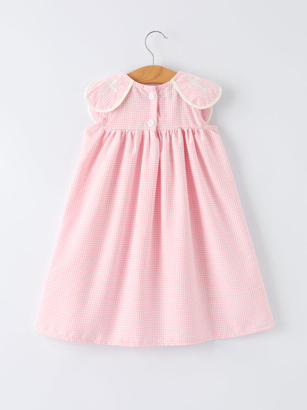 Pink gingham christening dress for girls with white-trimmed shoulder patches featuring cross embroidery, on hanger.