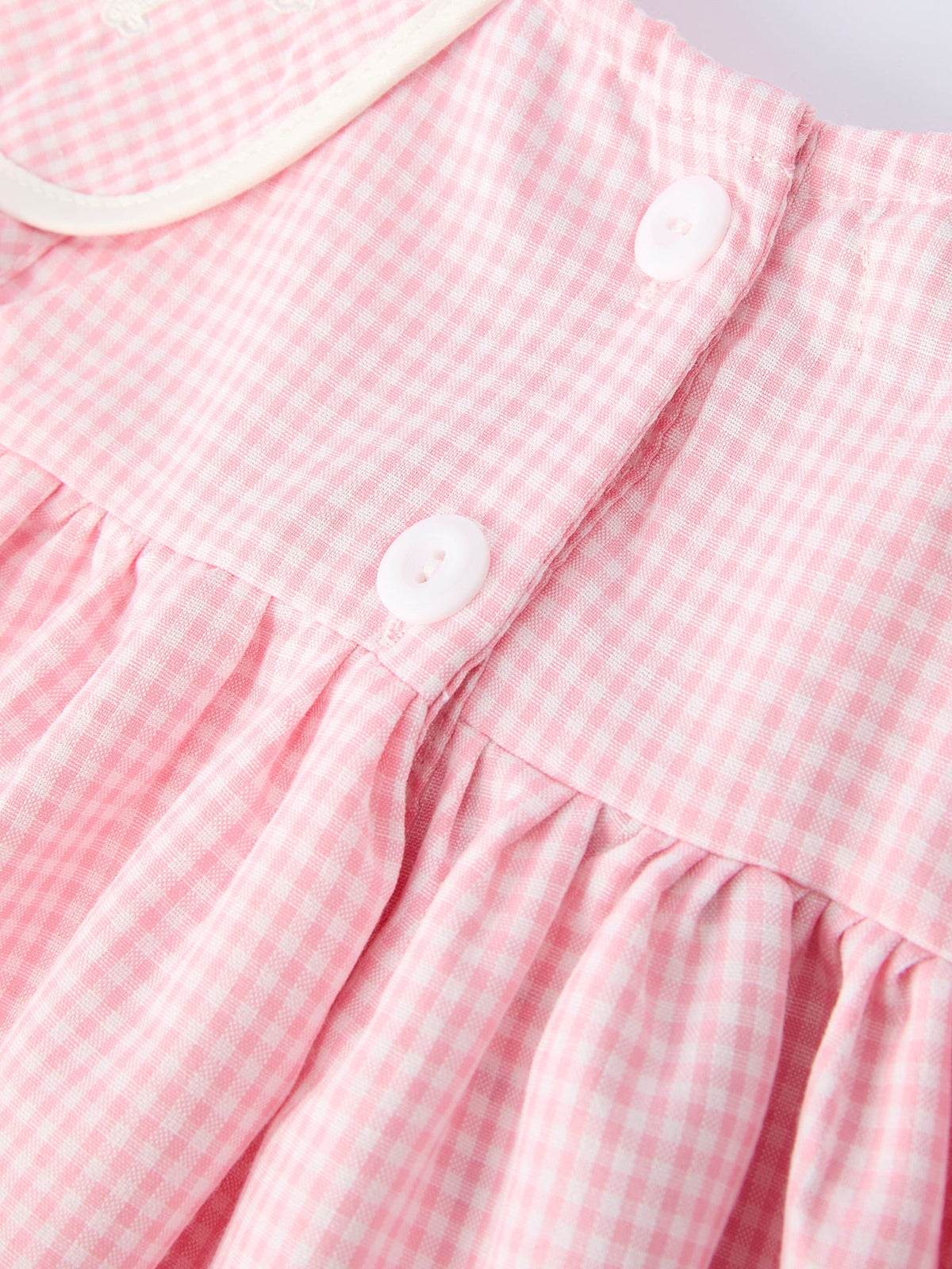 Close-up of pink gingham dress fabric with white buttons and gathered waist.
