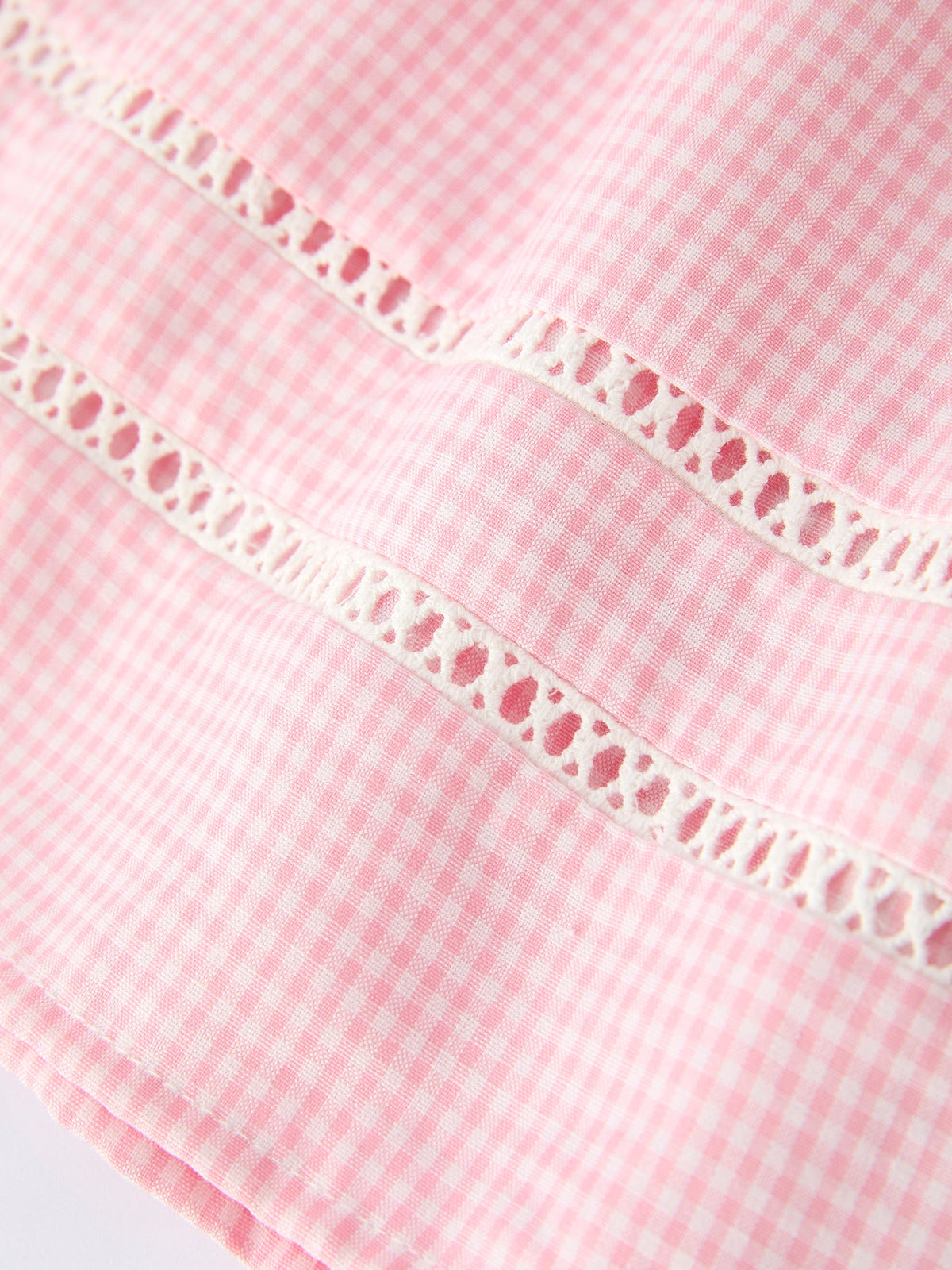 Close-up of pink gingham cotton fabric with white lace trim.