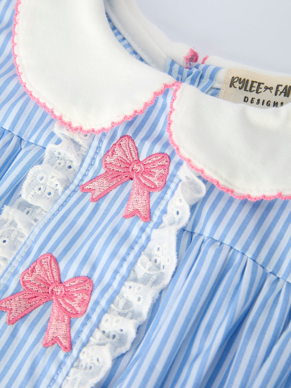 Blue striped romper for girls with petal Peter Pan collar, pink embroidered bows, and white lace trim.