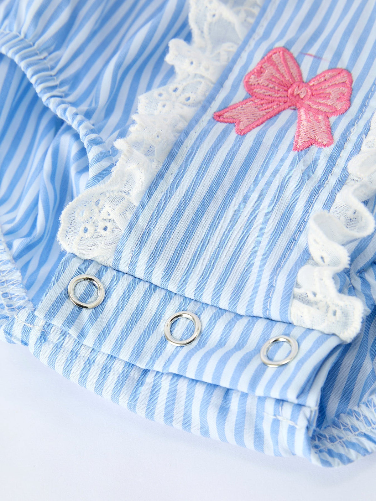 Blue striped romper fabric with pink embroidered bow and white lace trim.