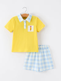 Yellow boys polo short set with pencil embroidery on a patch pocket, blue plaid collar, and matching light-blue gingham shorts.