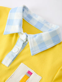 Blue and white pencil plaid collar over a yellow polo with white buttons and embroidery patch detail