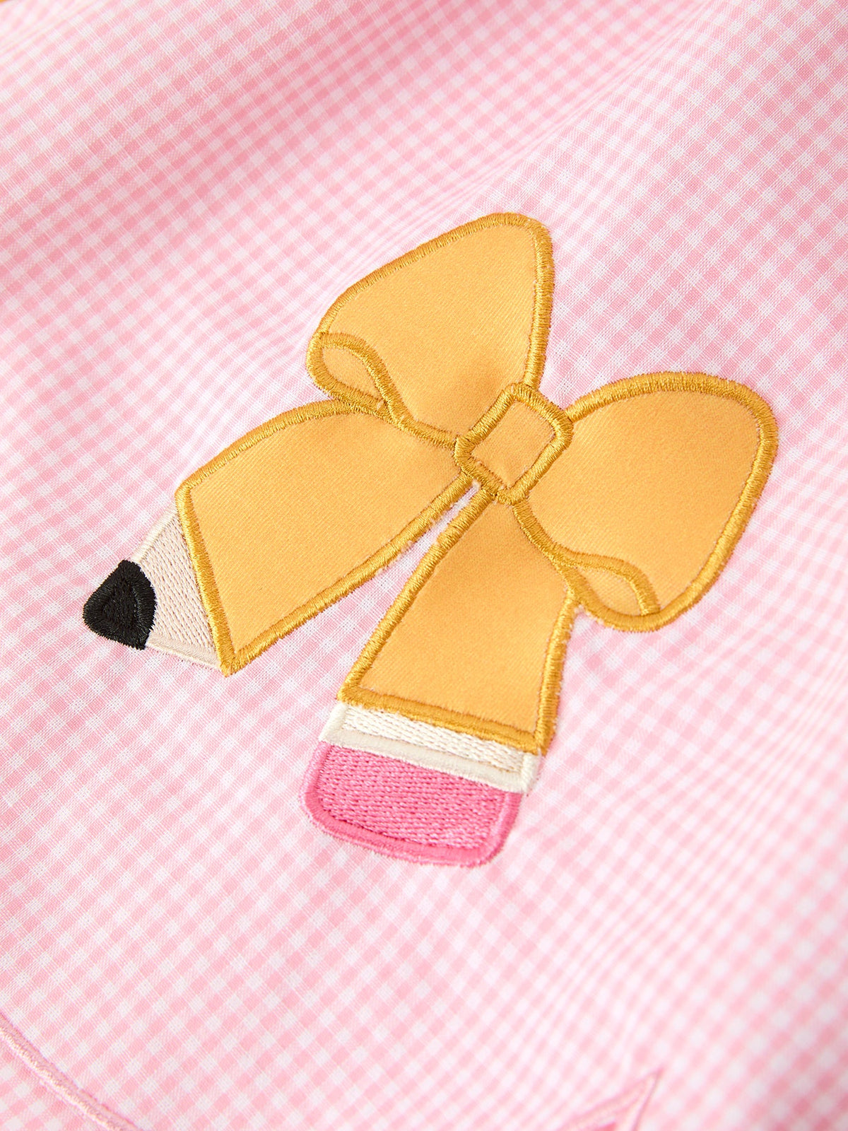 Highlighting the adorable bow applique on the Girls Back To School Pencil Twirl Dress, showcasing a pencil design in vibrant yellow against a pink checkered pattern.