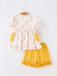Girls back-to-school pencil-bow print top with puff sleeves and yellow pockets, paired with mustard ruffle shorts set.