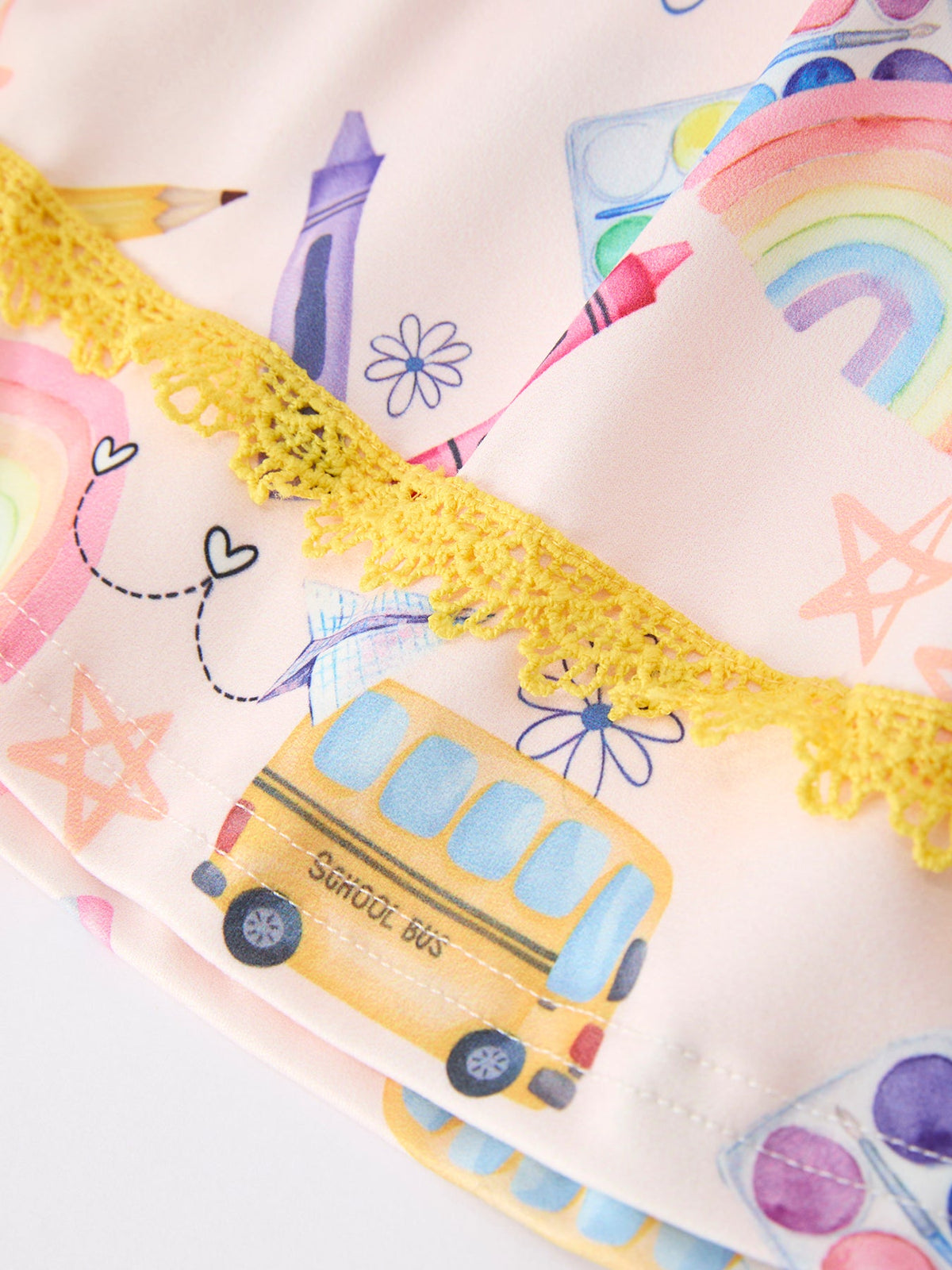 Close-up detail of the Girls Back To School Rainbow School Bus Ruffle Dress Leggings Set featuring colorful school bus, rainbow, and art supplies print, accented with yellow lace trim.