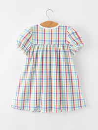 Back view of Girls Back To School Dog Plaid Twirl Dress with puff sleeves on a wooden hanger.
