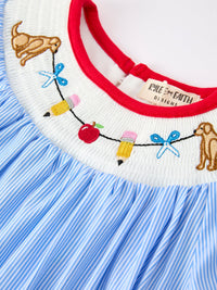 School-themed embroidery on neckline of a dress with pencil, apple, and scissors; red trim and blue stripes.
