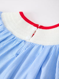 Close-up of a blue and white striped dress with a white smocked collar, red trim, and two white buttons.