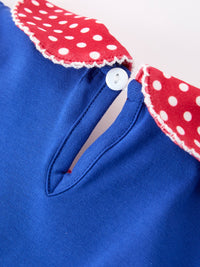 Blue dress close-up: red polka-dot petals collar with white trim and a white button.