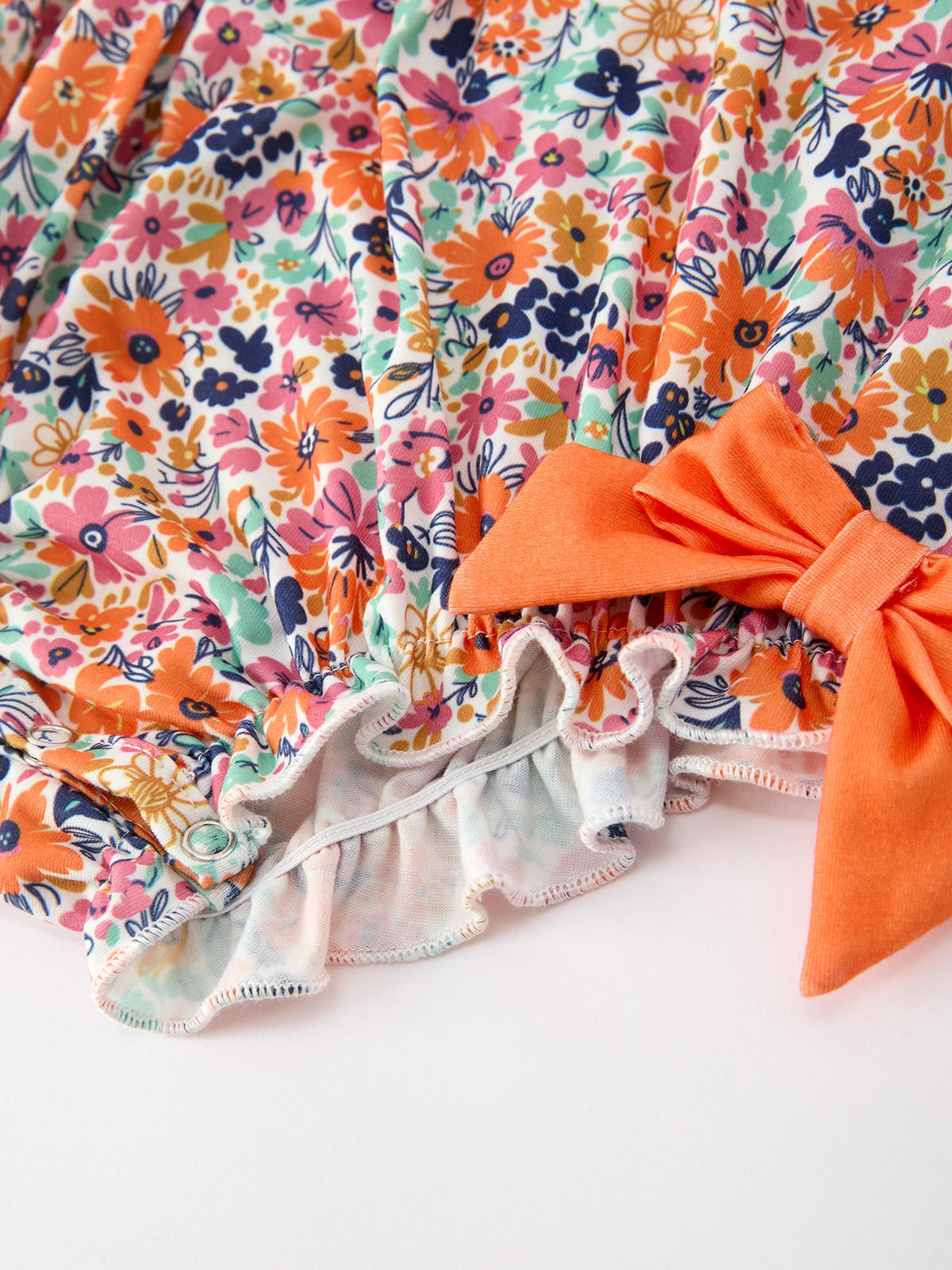 Orange floral romper for girls with petals collar, eyelet trim, and bow accent.