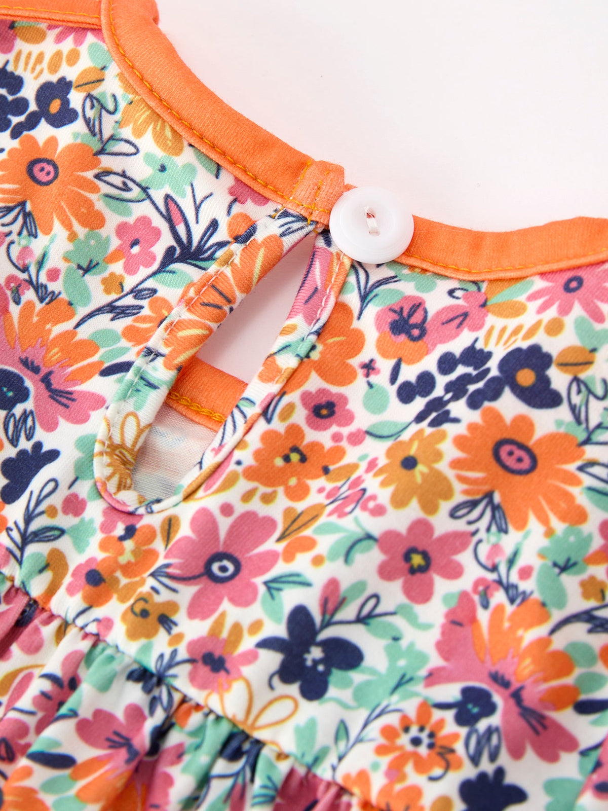 Close-up of orange trim on floral romper with petals collar and button detail