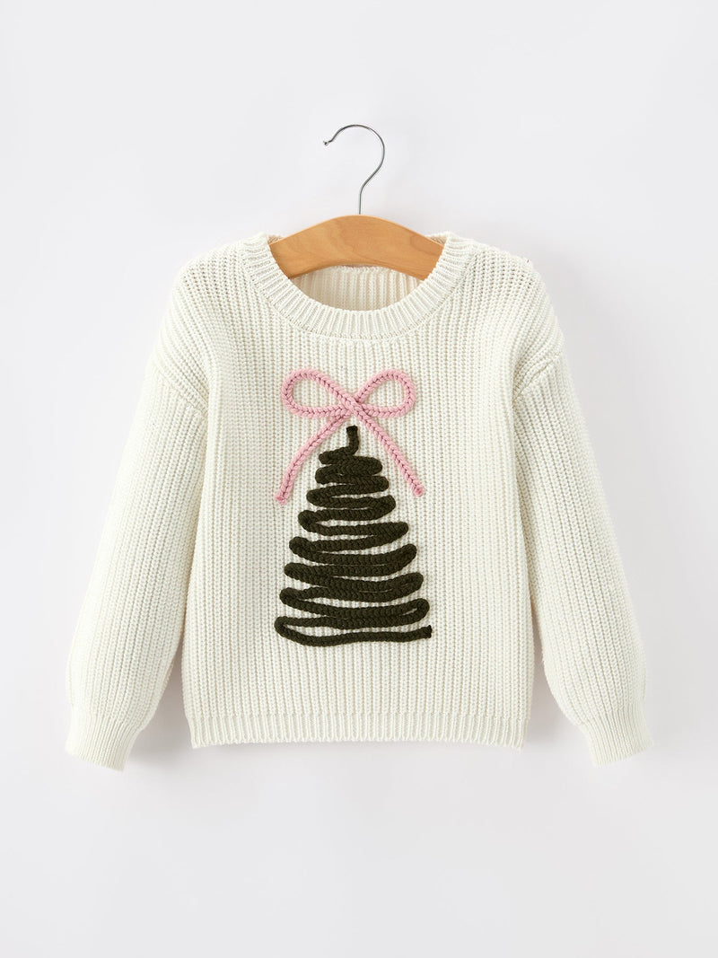An off-white ribbed knit sweater hanging on a wooden hanger against a light gray background. The sweater features a Christmas tree motif with a pink bow on the front.