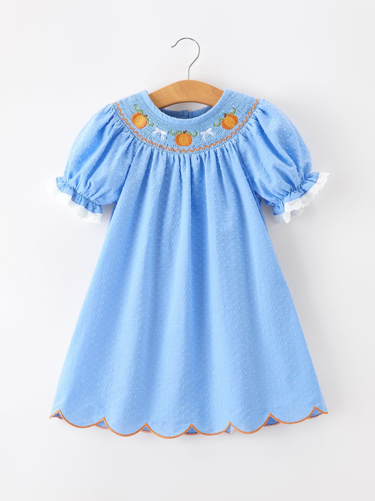 Blue baby dress with pumpkin embroidery on yoke, smock styling, lace-trimmed puff sleeves, scalloped hem.