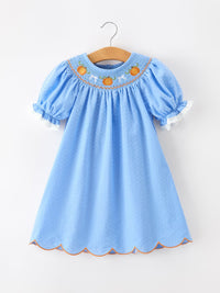 Blue baby dress with pumpkin embroidery on yoke, smock styling, lace-trimmed puff sleeves, scalloped hem.