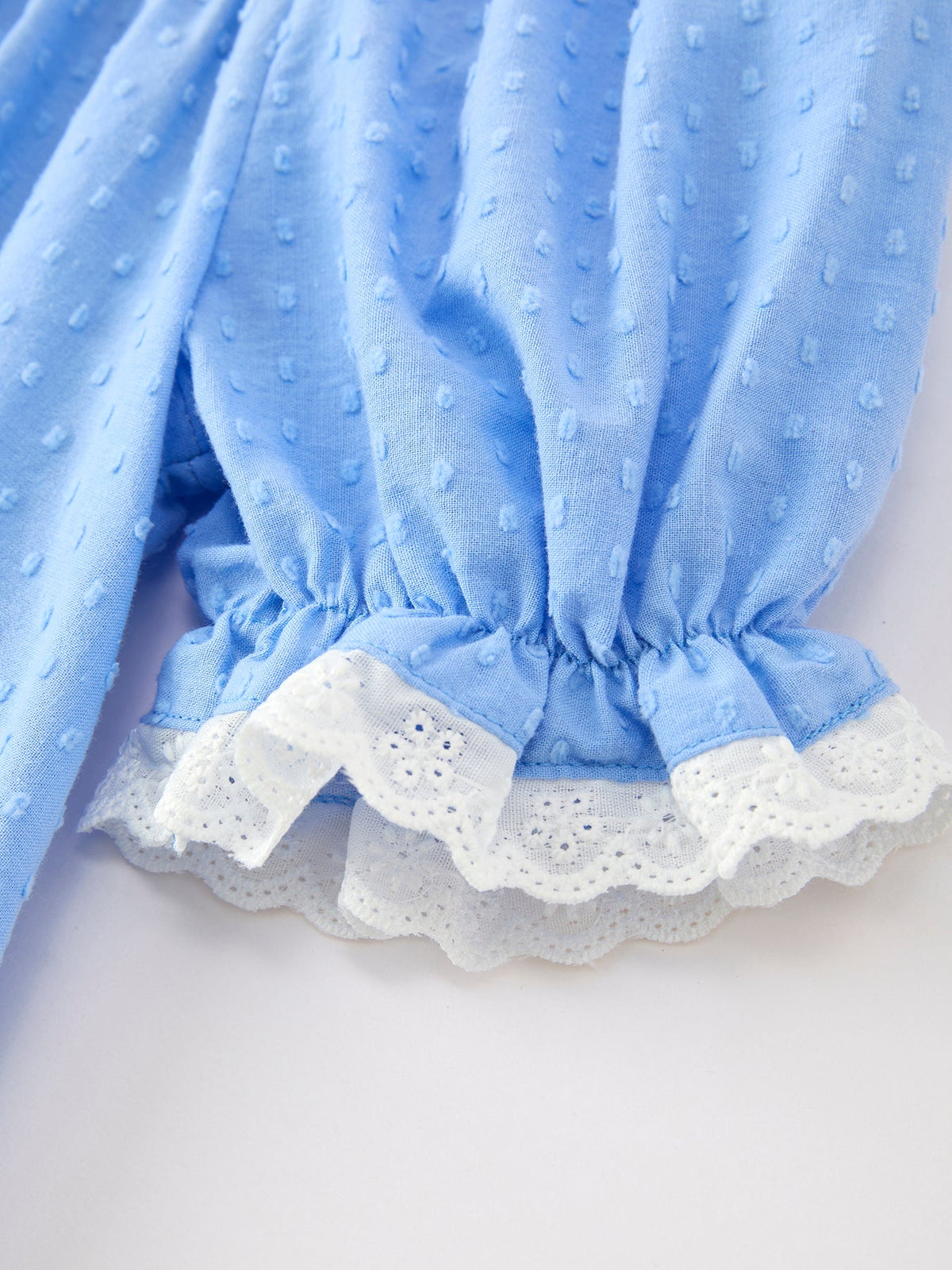 Blue baby dress close-up with dotted fabric and white lace trim, smocked waist detail.