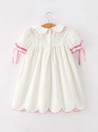 Ivory girls christening dress with pink scalloped collar, puff sleeves, ribbon ties, and scalloped hem for aGraceful baptism look.