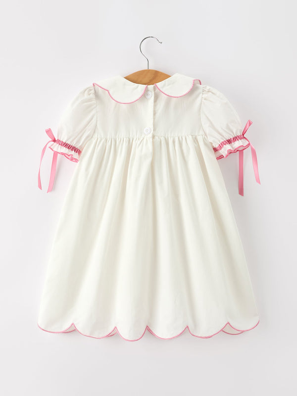 Ivory girls christening dress with pink scalloped collar, puff sleeves, ribbon ties, and scalloped hem for aGraceful baptism look.
