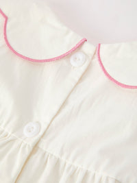 Ivory christening dress with pink embroidered scalloped collar and white button closure, featuring soft fabric and elegant details for a graceful look.