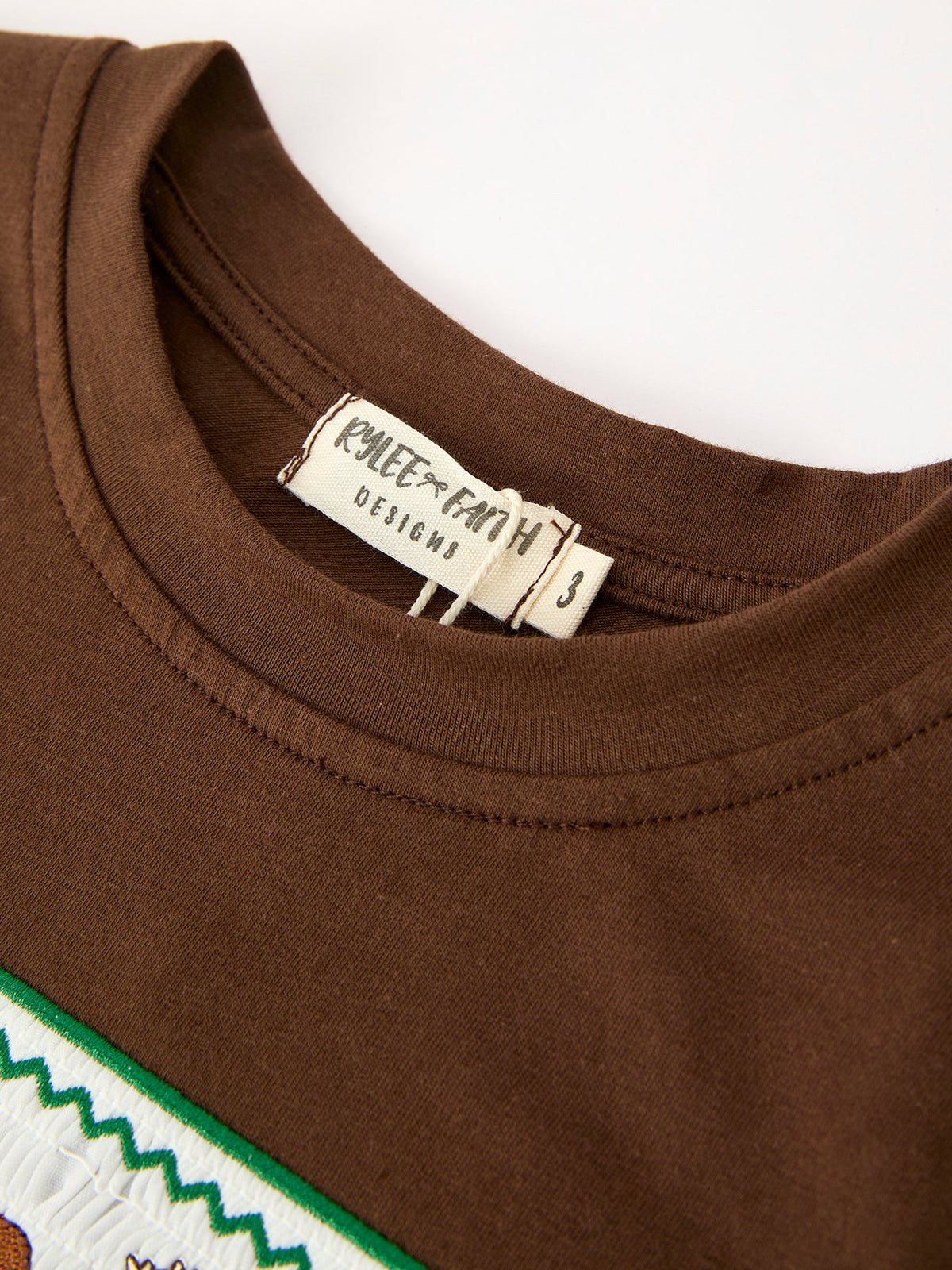 Inner neck label reading Rylee Faith Designs size 3 stitched into brown ribbed crew neckline collar
