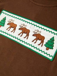 Macro shot of white smocked chest patch with three brown moose, green pine trees, and zigzag border stitching