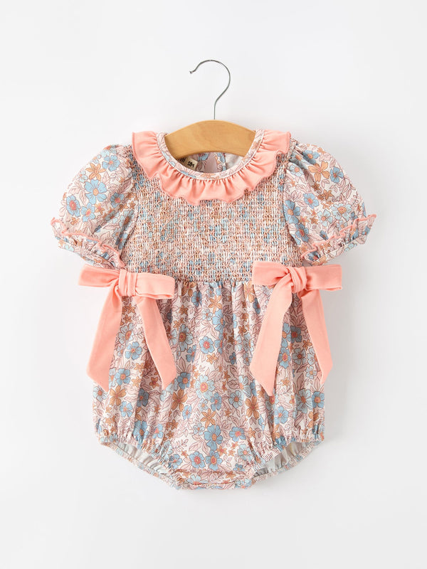 Fall floral baby romper with smocked bodice, pink ruffle neckline, and pink bow accents.
