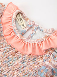 Fall floral baby romper with smocked bodice, ruffle neck, and bow accents in pink pastel print.