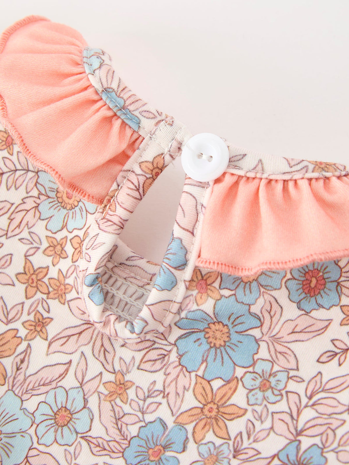 Close-up of Fall floral baby romper fabric with smocked ruffle neck and button closure.