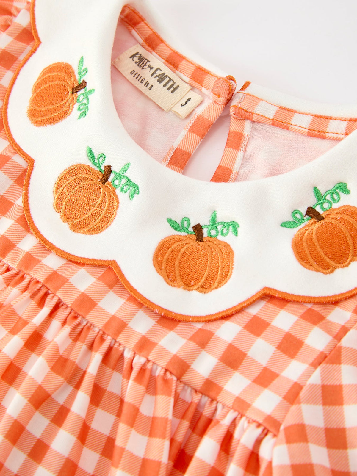 Orange gingham girls dress featuring a white scalloped collar with embroidered pumpkins, puff sleeves, and festive fall details.