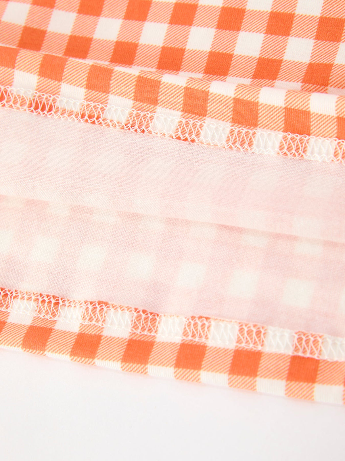 Close-up of orange and white gingham fabric with delicate white stitching, featuring soft pink plaid detailing for a fall girls dress.
