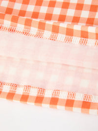 Close-up of orange and white gingham fabric with delicate white stitching, featuring soft pink plaid detailing for a fall girls dress.