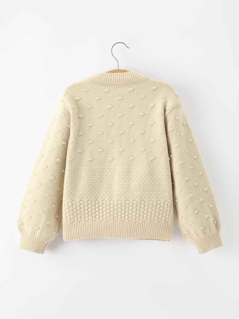 Back of cream kids knit cardigan featuring textured dot pattern and ribbed hem for festive holiday wear.