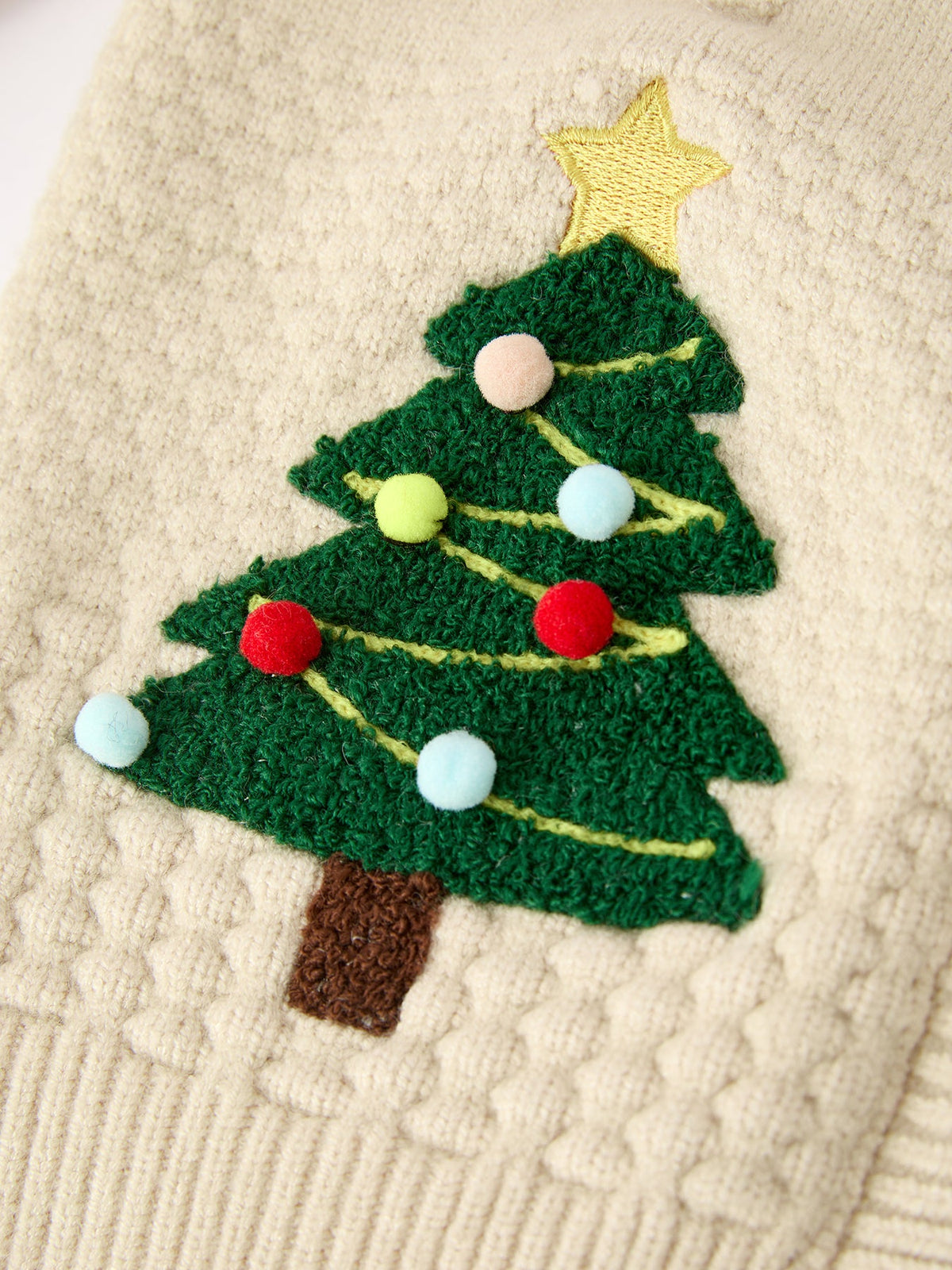 Green felt Christmas tree applique with colorful pom-poms and gold star on beige knit sweater