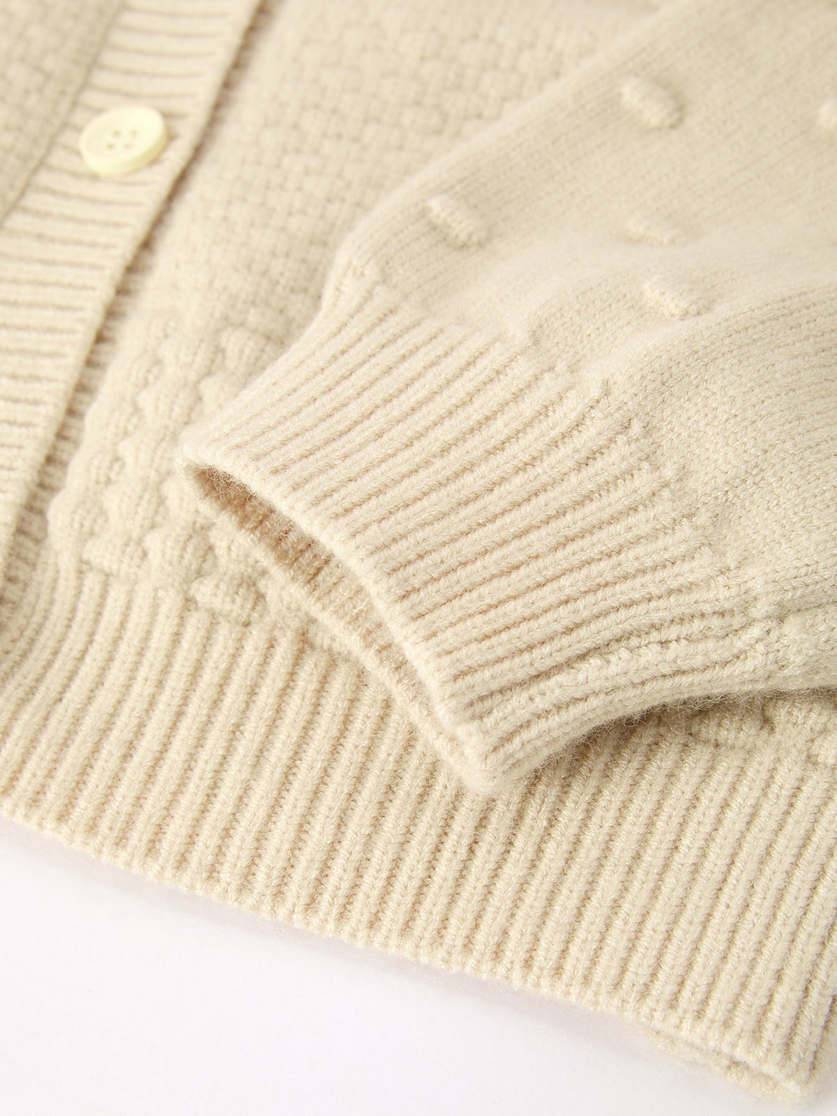 Cream knit cardigan detail showing ribbed cuff, button front, and soft textured fabric for kids' holiday sweater.