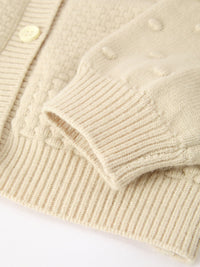 Cream knit cardigan detail showing ribbed cuff, button front, and soft textured fabric for kids' holiday sweater.